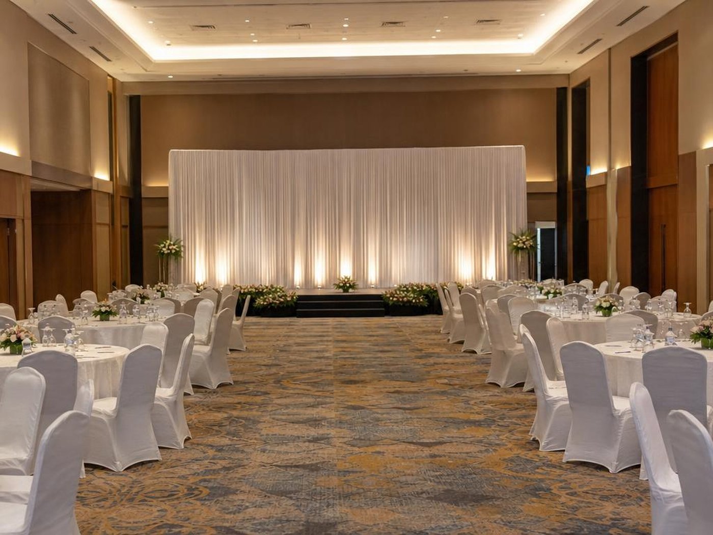 Hall gala dinner dengan uplighting panggung dan tata kursi rapi