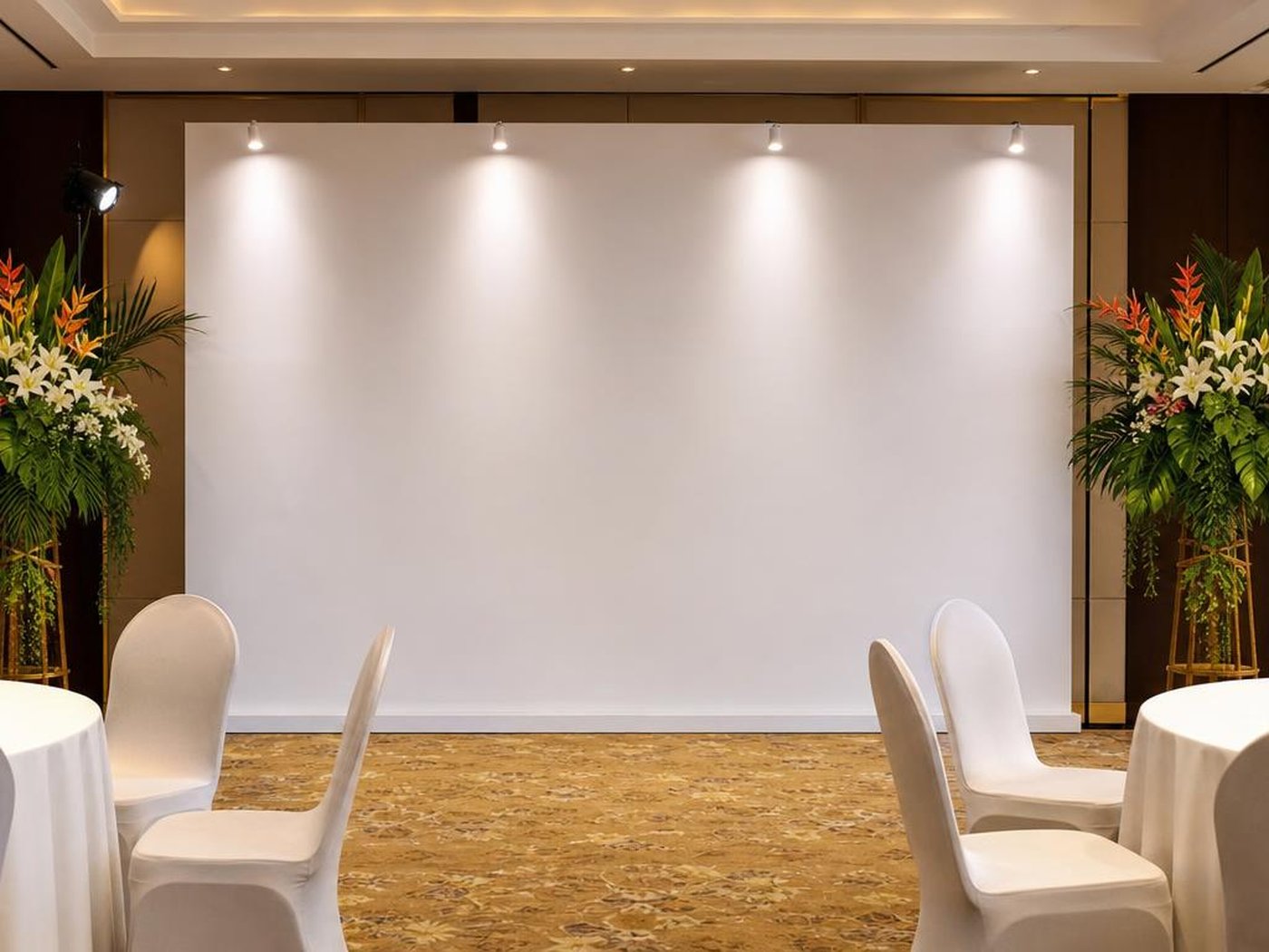 Backdrop blanko berpencahayaan sorot dengan stand bunga tropis di ruang acara hotel