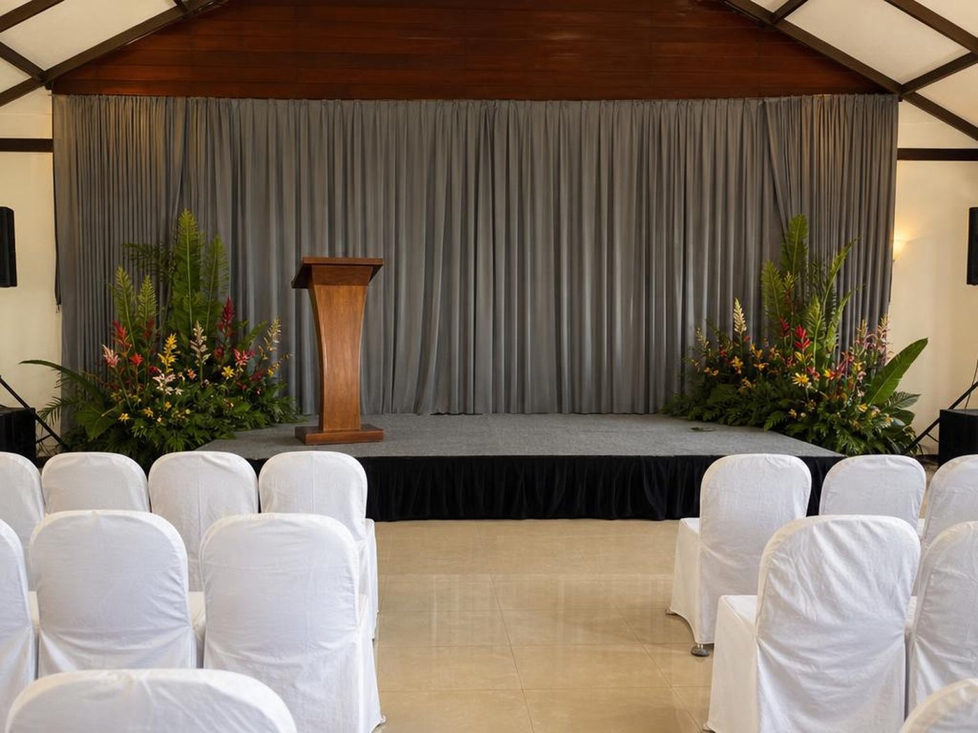 Panggung seminar sederhana dengan drapery abu-abu, podium kayu, dan sound system di hall acara