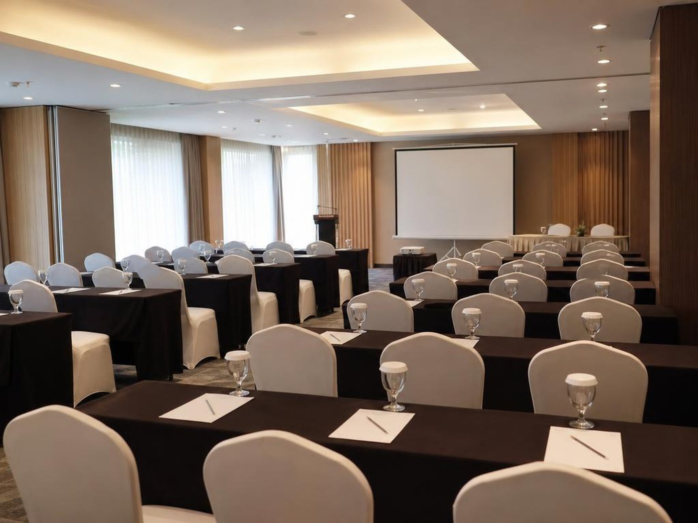 Ruang meeting korporat dengan kursi bersarung putih dan layar proyektor