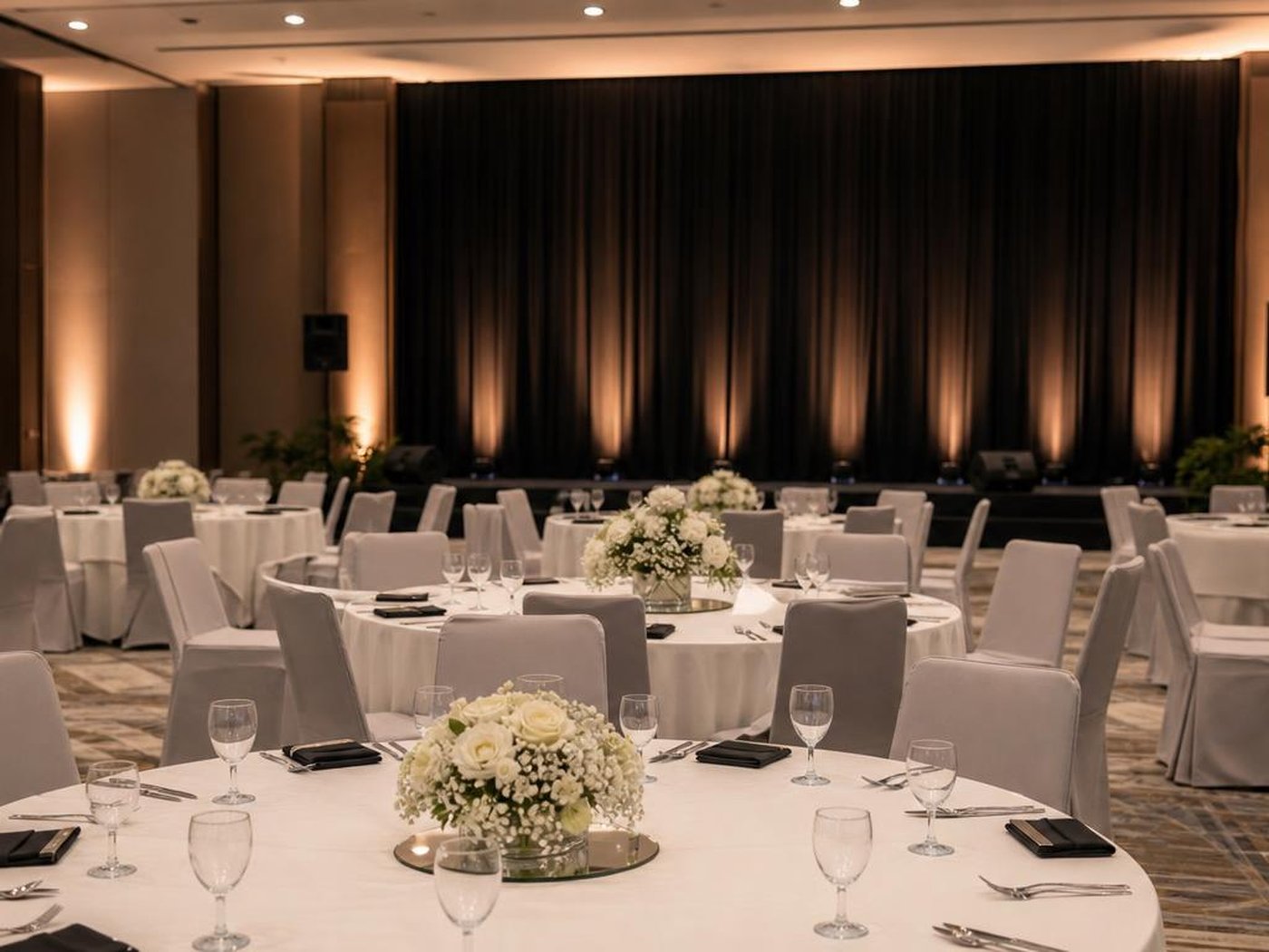 Set up gala dinner korporat dengan meja bundar dan panggung berlatar kain hitam