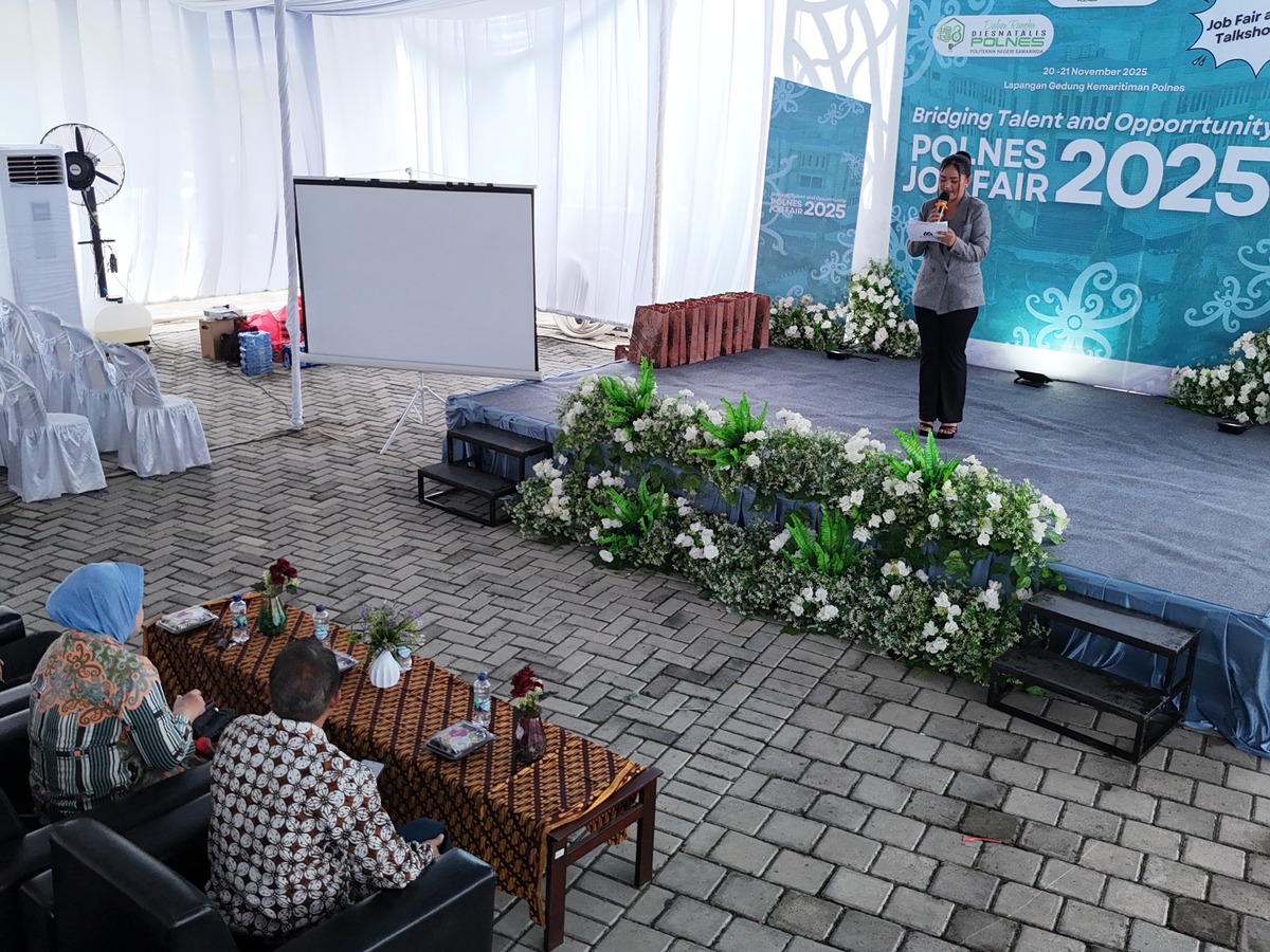 Panggung acara dengan backdrop cetak, layar proyeksi, dekorasi bunga, dan area tamu.
